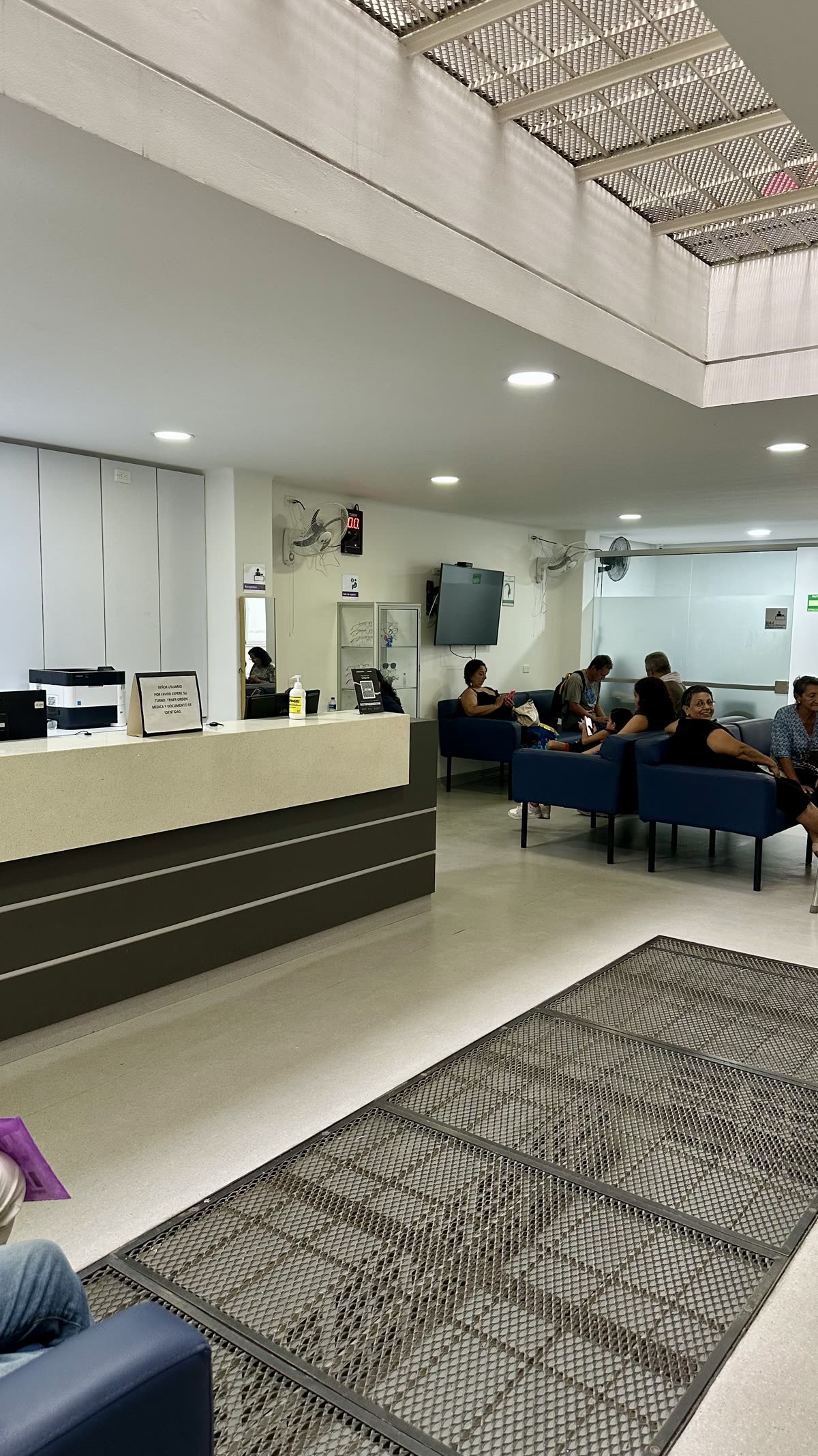 Sala de espera amplia con sillas, pantalla informativa y mostrador de atención.